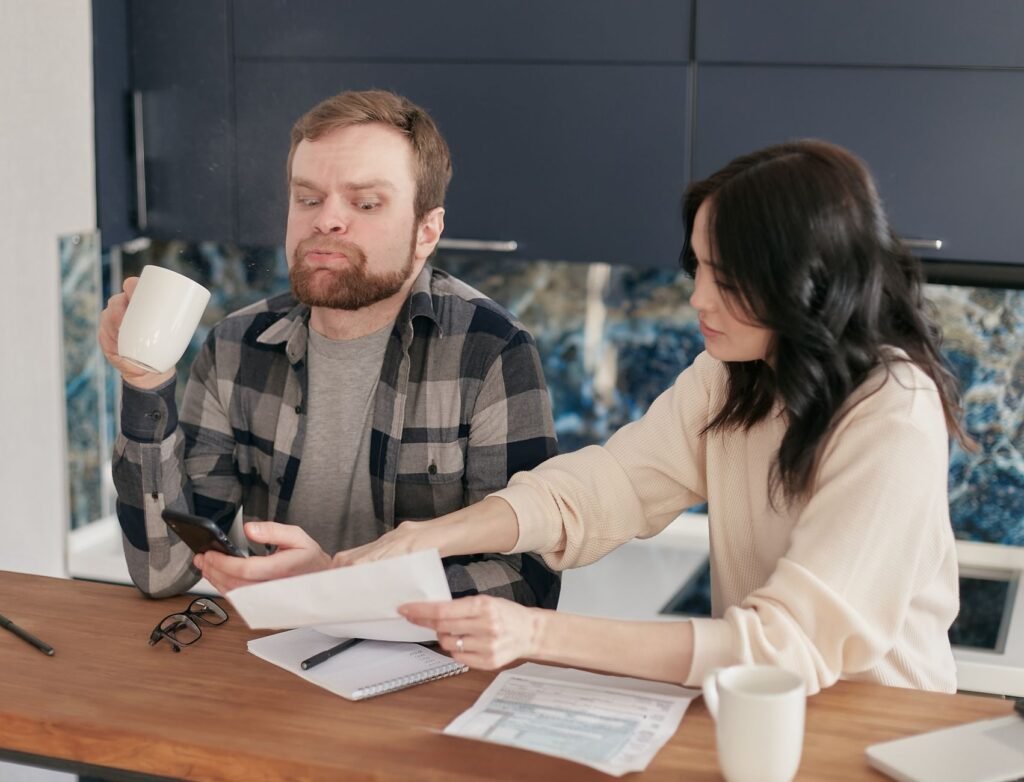 A couple looks worried as they review bills at their kitchen table, reflecting financial concerns