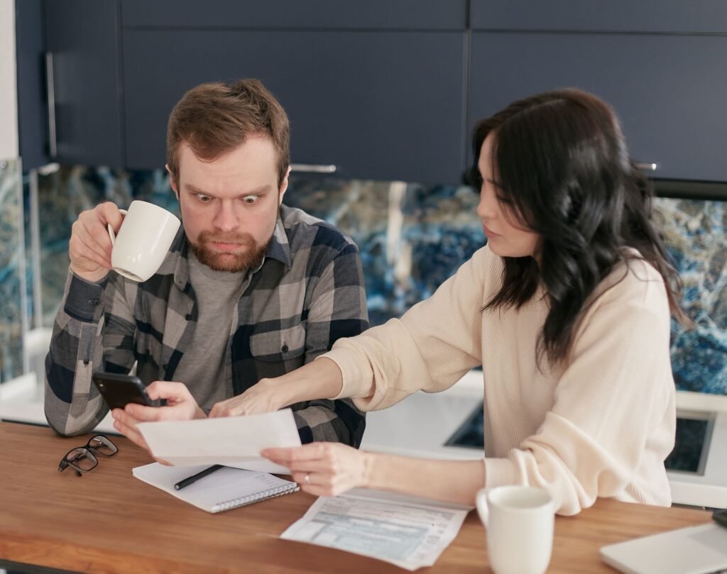 A couple reviews household bills in a kitchen, appearing concerned and focused