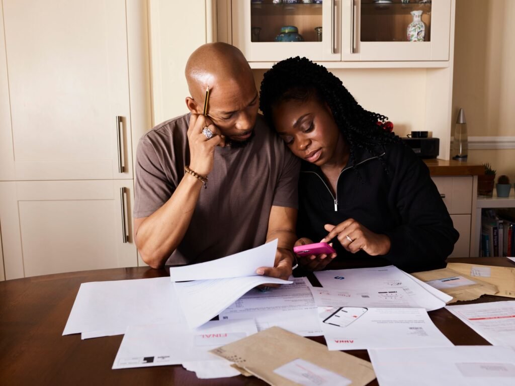 A couple sits at a table managing domestic finances, evaluating documents and using a smartphone
