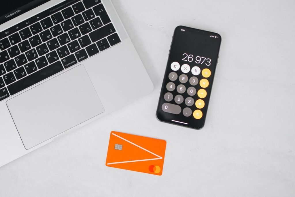 A laptop, smartphone displaying calculator, and credit card on a white table