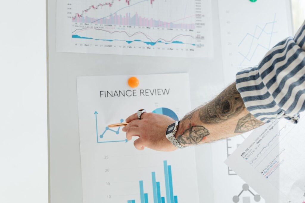 A person with tattooed arms presenting financial data using charts and graphs on a whiteboard