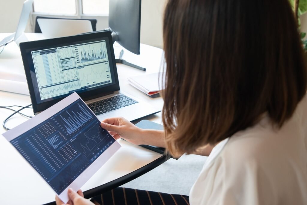 A professional woman analyzes financial charts on a laptop and paper for business insights