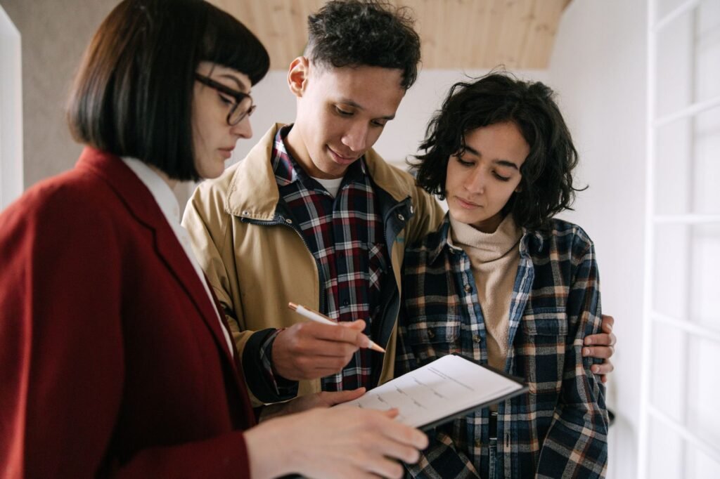 A young couple consults with a real estate agent about documents inside an apartment
