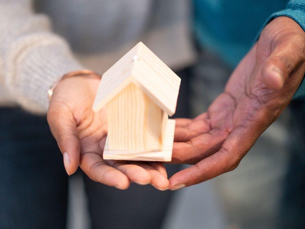 Close-up of hands holding a small wooden house, representing real estate and new home ownership