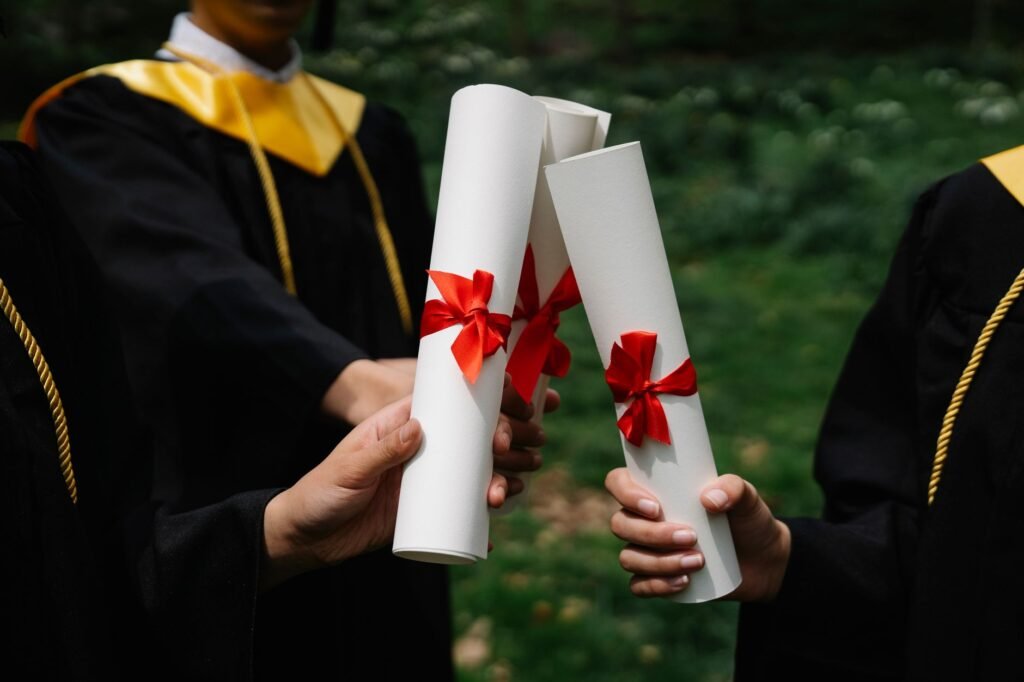 Group of graduates holding diplomas with red ribbons during a ceremony outdoors