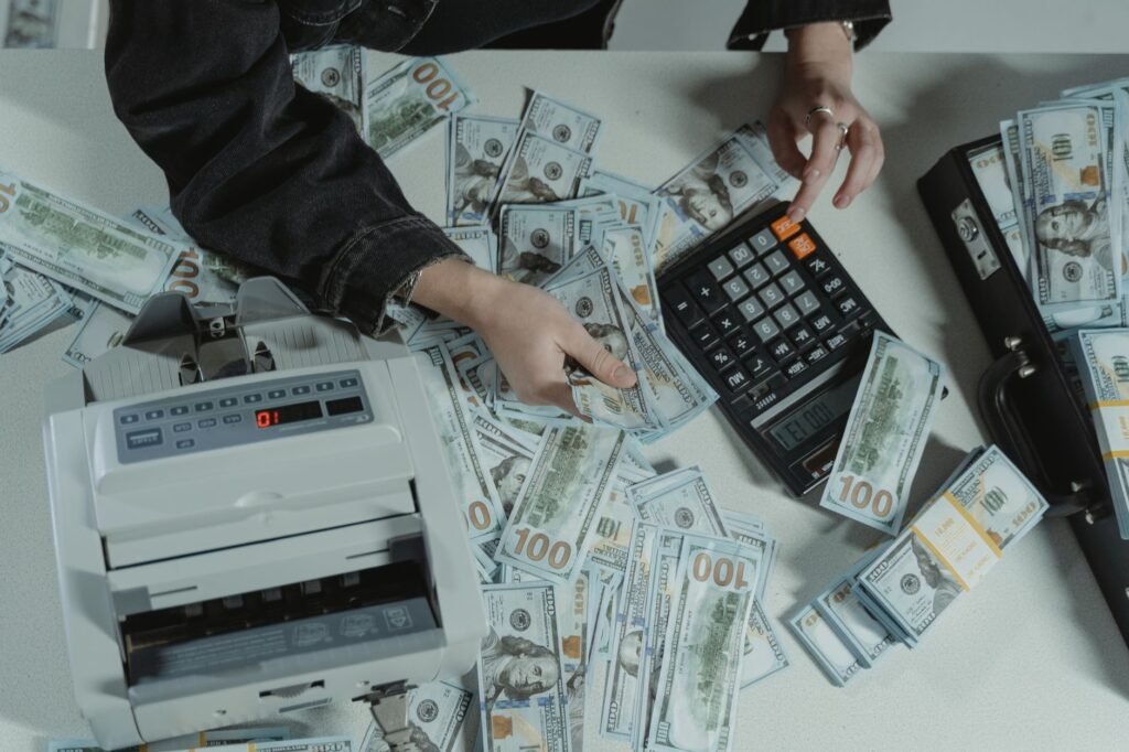 Hands counting 100 dollar bills using a calculator and money counter on a table