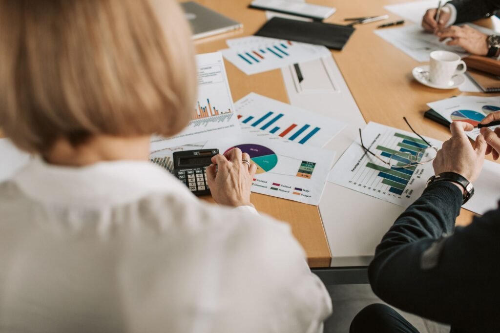 Overhead view of professionals discussing financial graphs and using calculators in an office setting