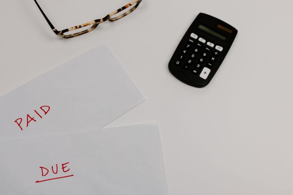 Top view of financial papers labeled 'Paid' and 'Due' beside a calculator and glasses