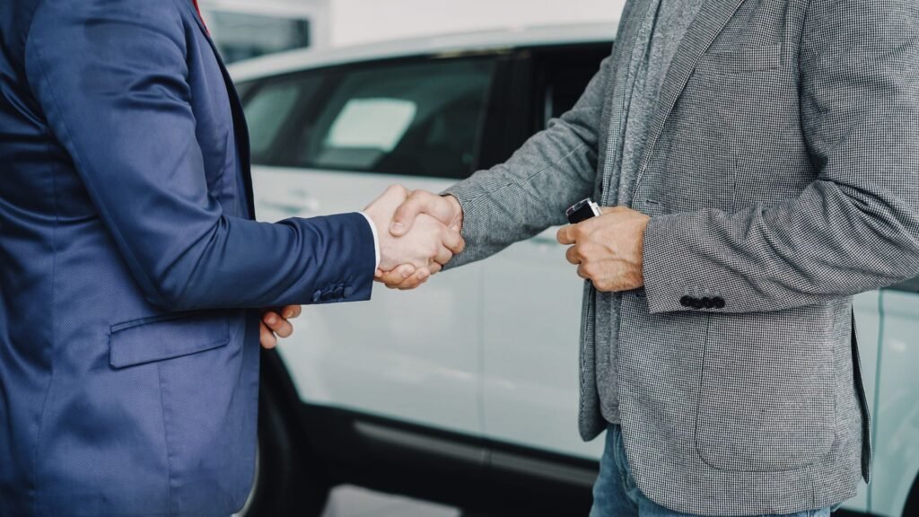 Two businessmen shaking hands in a car dealership, sealing a deal