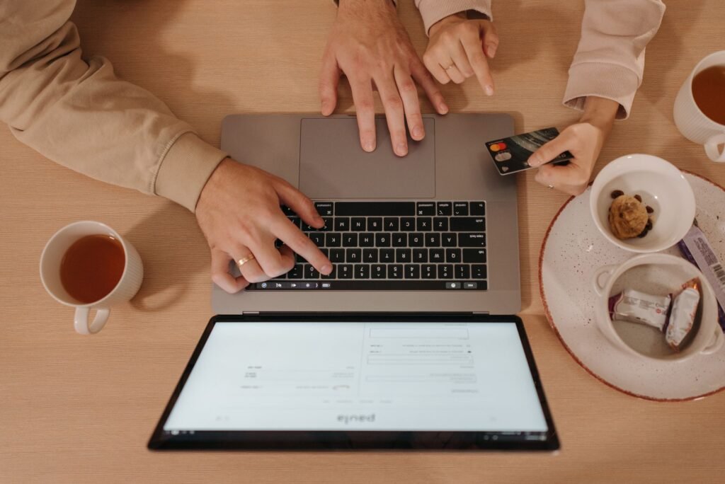 Two people using a laptop for online shopping with a credit card, seen from above
