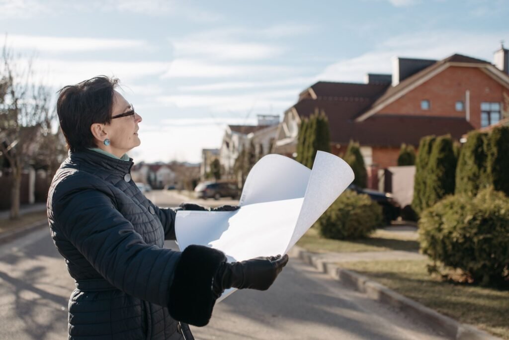 Woman in a blue jacket reviewing architectural plans outdoors on a sunny day