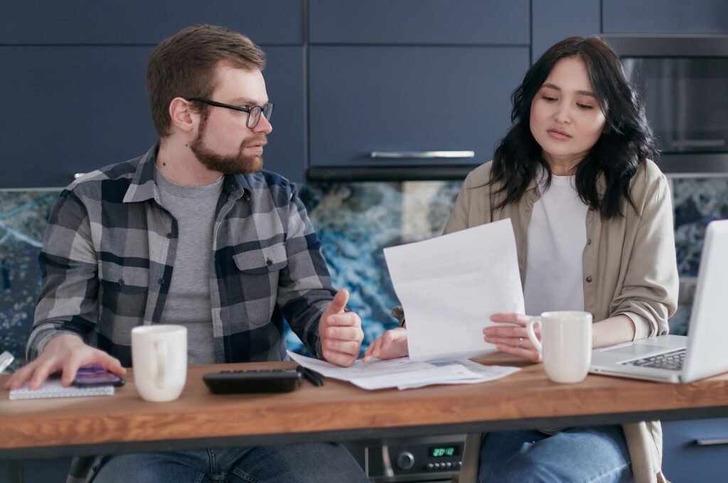 A couple sits at a table reviewing financial documents, looking concerned and focused
