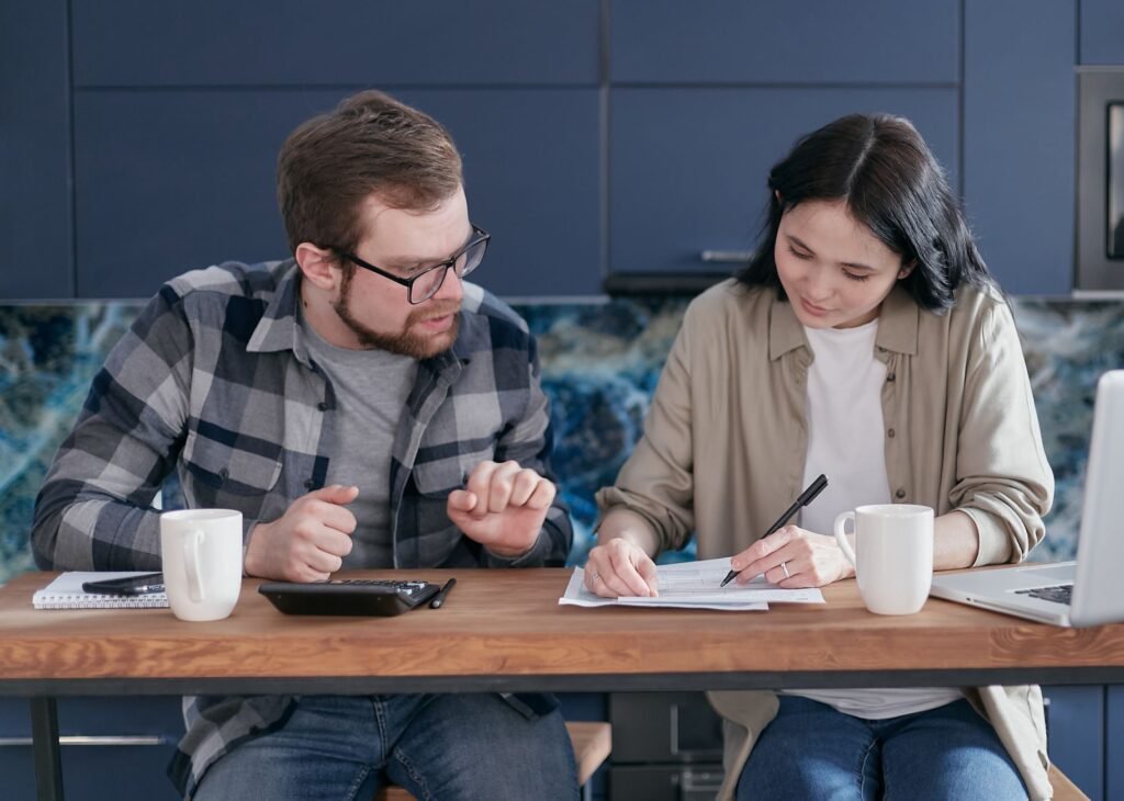 A couple sitting at a table managing their finances with a laptop and calculator, appearing focused