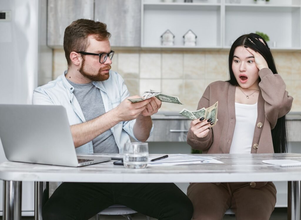 A shocked couple sitting at a table counting cash, illustrating financial surprise