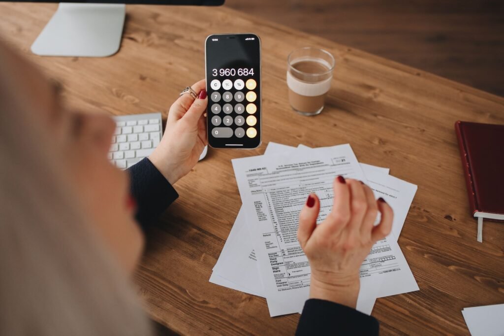 A woman calculates on her smartphone while working with documents at a desk