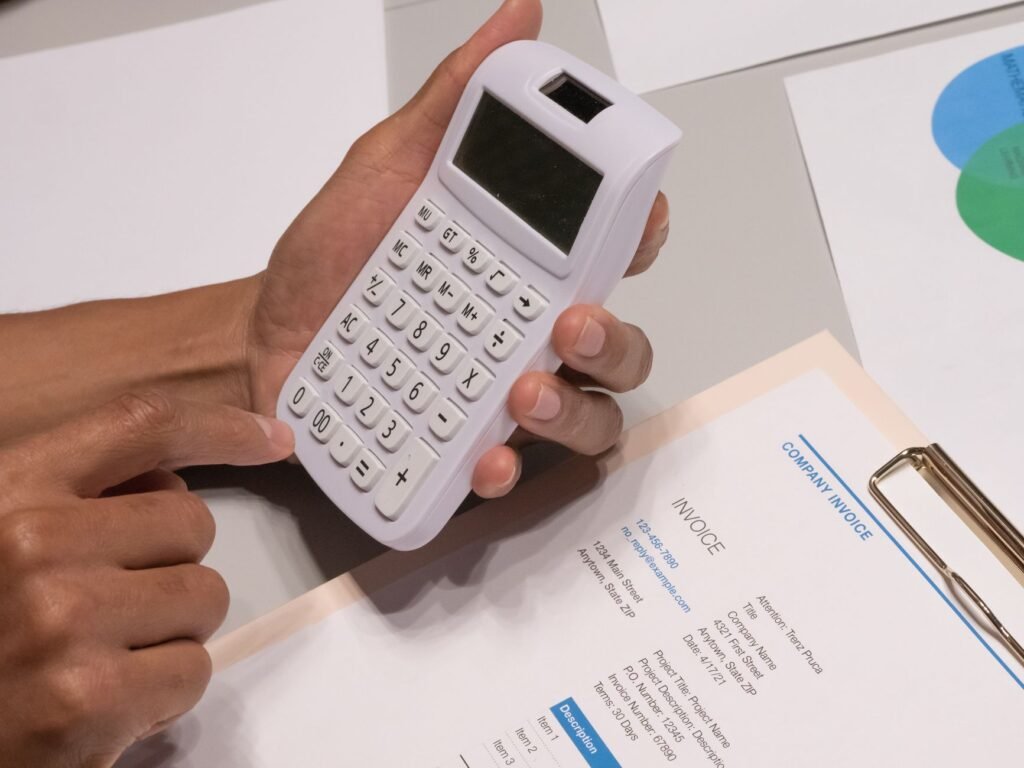 Close-up of hands using a calculator next to a company invoice, depicting a financial calculation concept