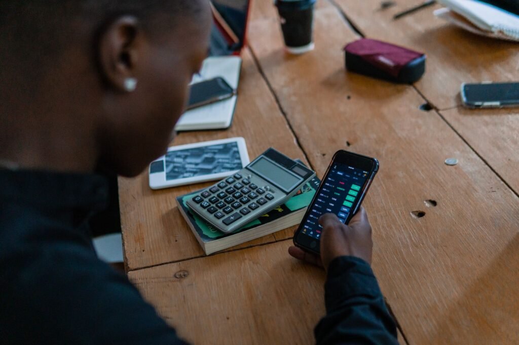 Close-up of individual using smartphone for financial data analysis, calculator nearby on wooden table