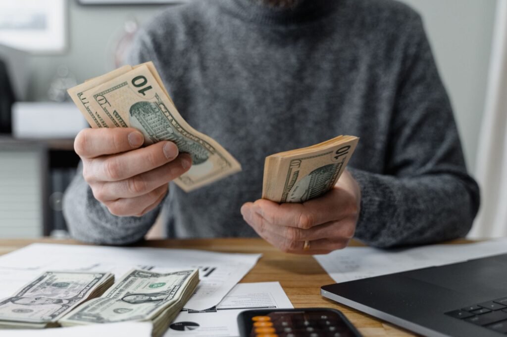 Close-up of person counting cash with a calculator and paperwork on a desk