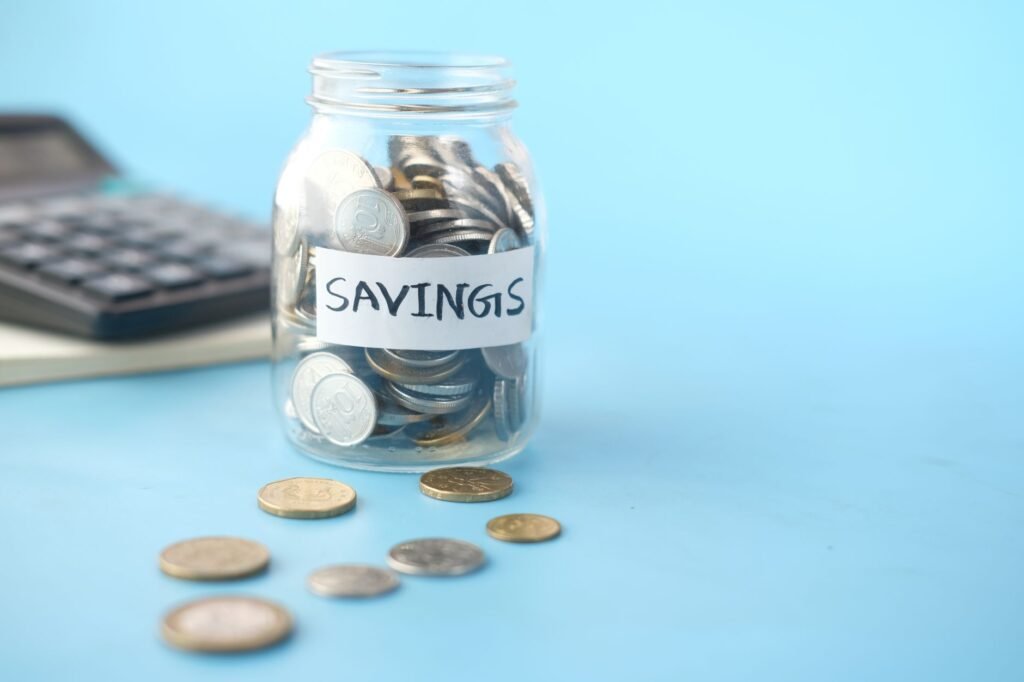 Glass jar labeled 'Savings' filled with coins, beside a calculator on a blue background