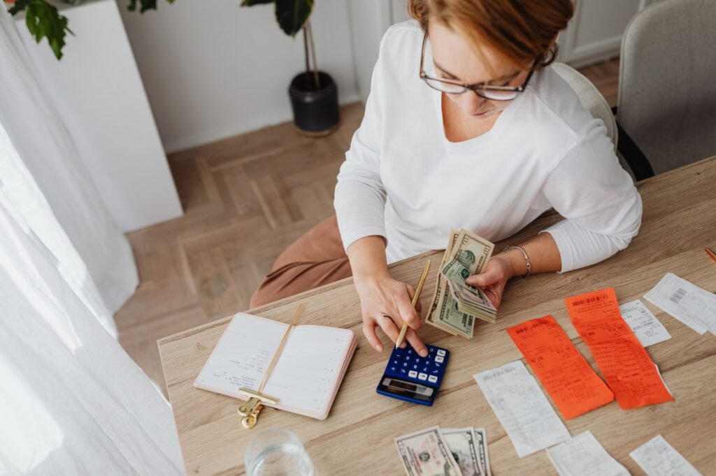 Top view of a woman managing finances with a calculator, cash, and bills in a home setting