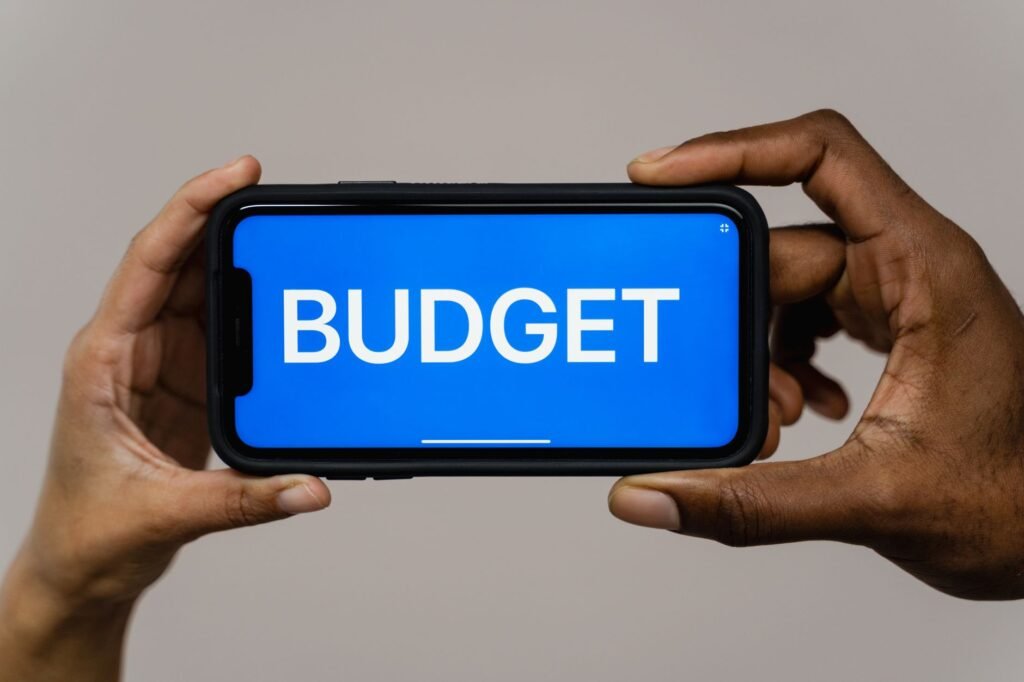 Two hands hold a smartphone displaying the word 'budget' on a blue screen, symbolizing financial planning