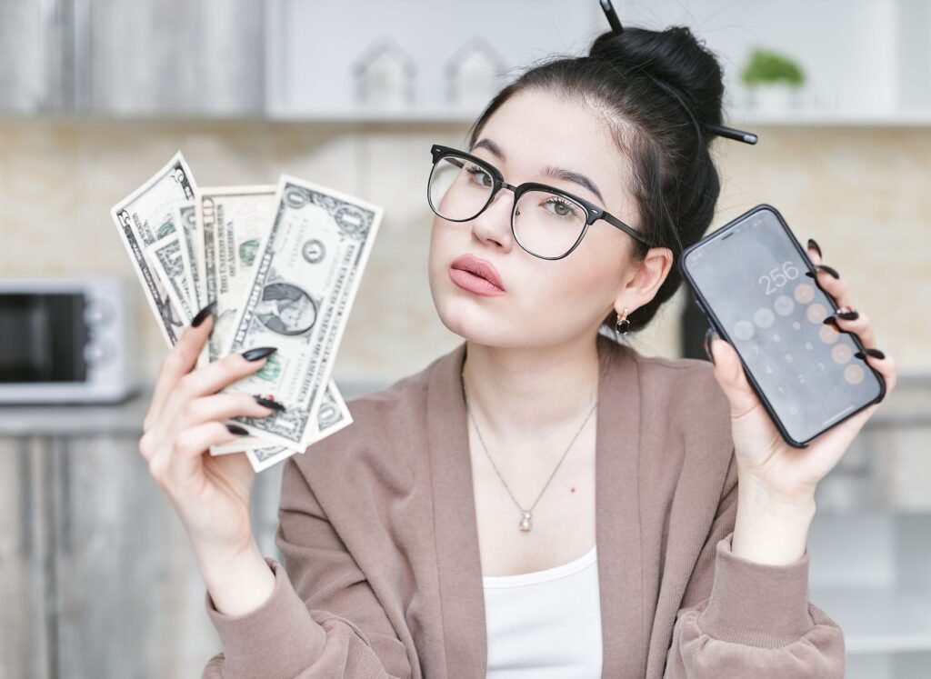 Woman holding cash and smartphone displaying calculator